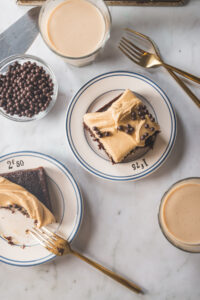 A square slice of A chocolate sheet cake with peanut butter frosting topped with chocolate crunch balls on a small white plate with blue stripes